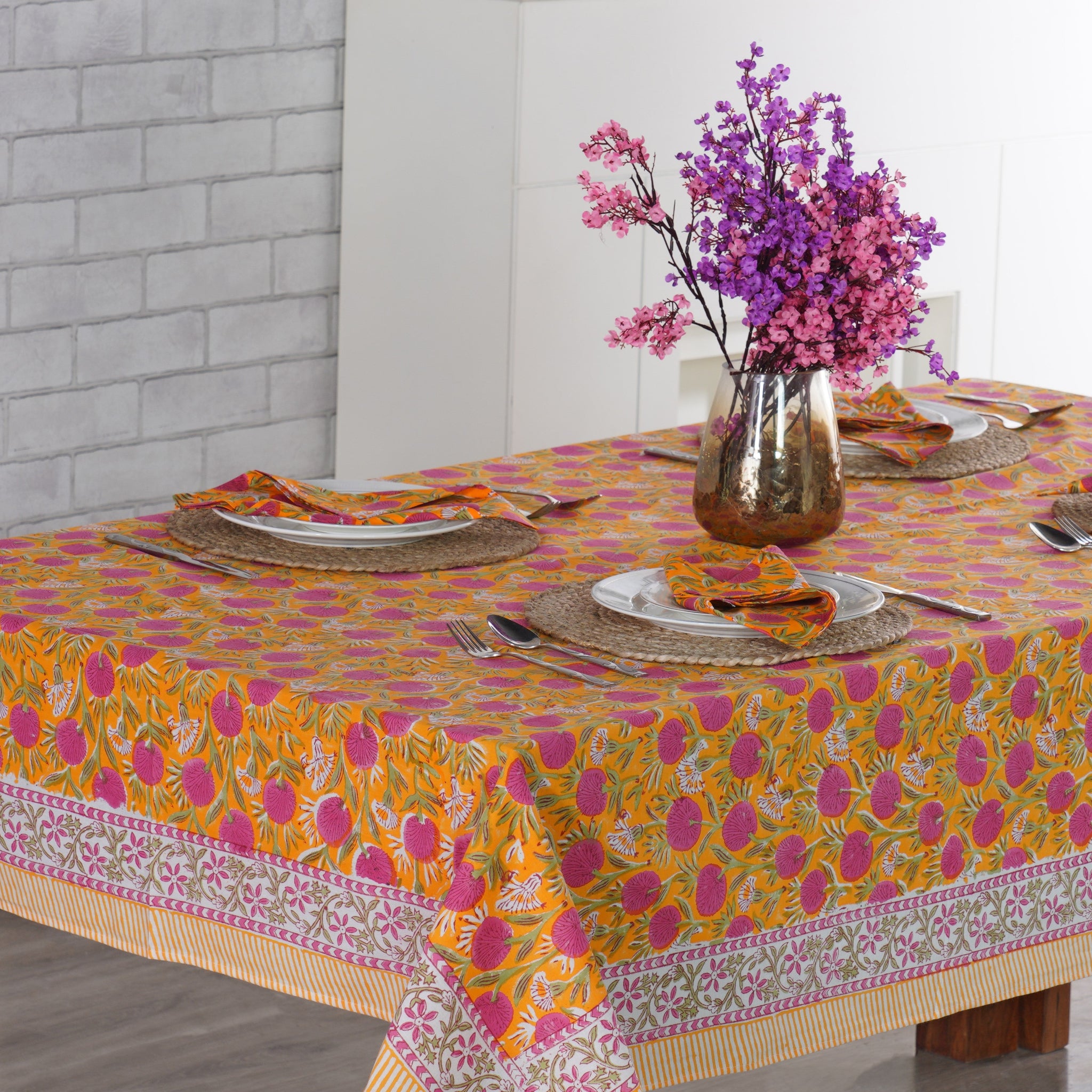 Dining table set with a colorful tablecloth, plates, and flowers.