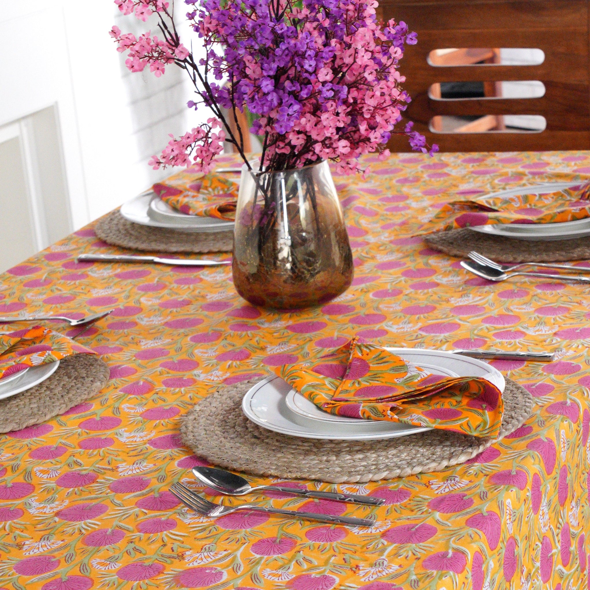 Table setting with a colorful floral tablecloth, plates, and cutlery.