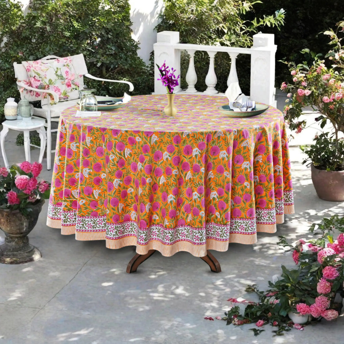 Outdoor setting with a table covered by a colorful floral tablecloth, surrounded by potted plants.