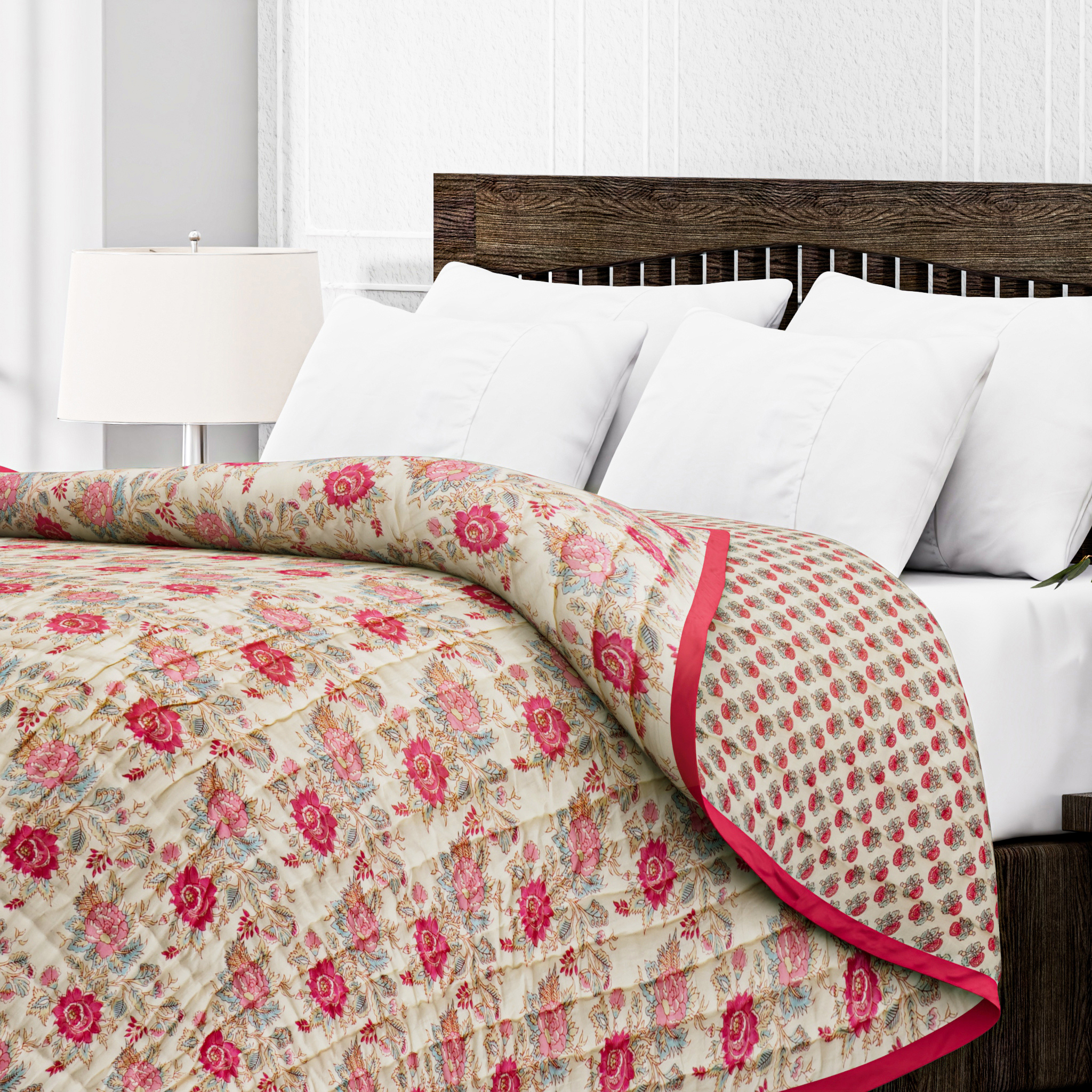 Floral quilt with pink and red patterns on a bed with white pillows and wooden headboard.