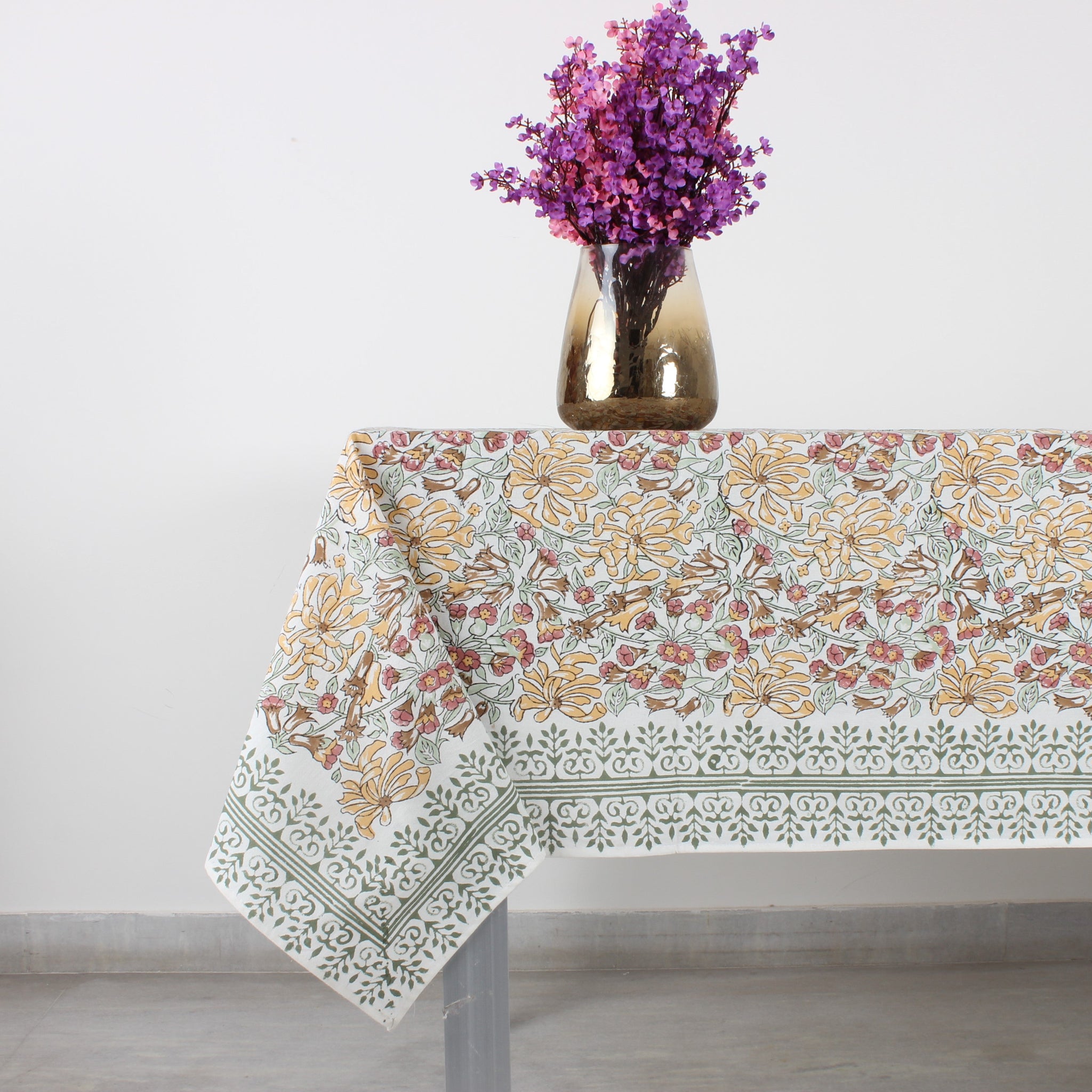 Floral patterned tablecloth on a table with a vase of purple flowers on a light gray background