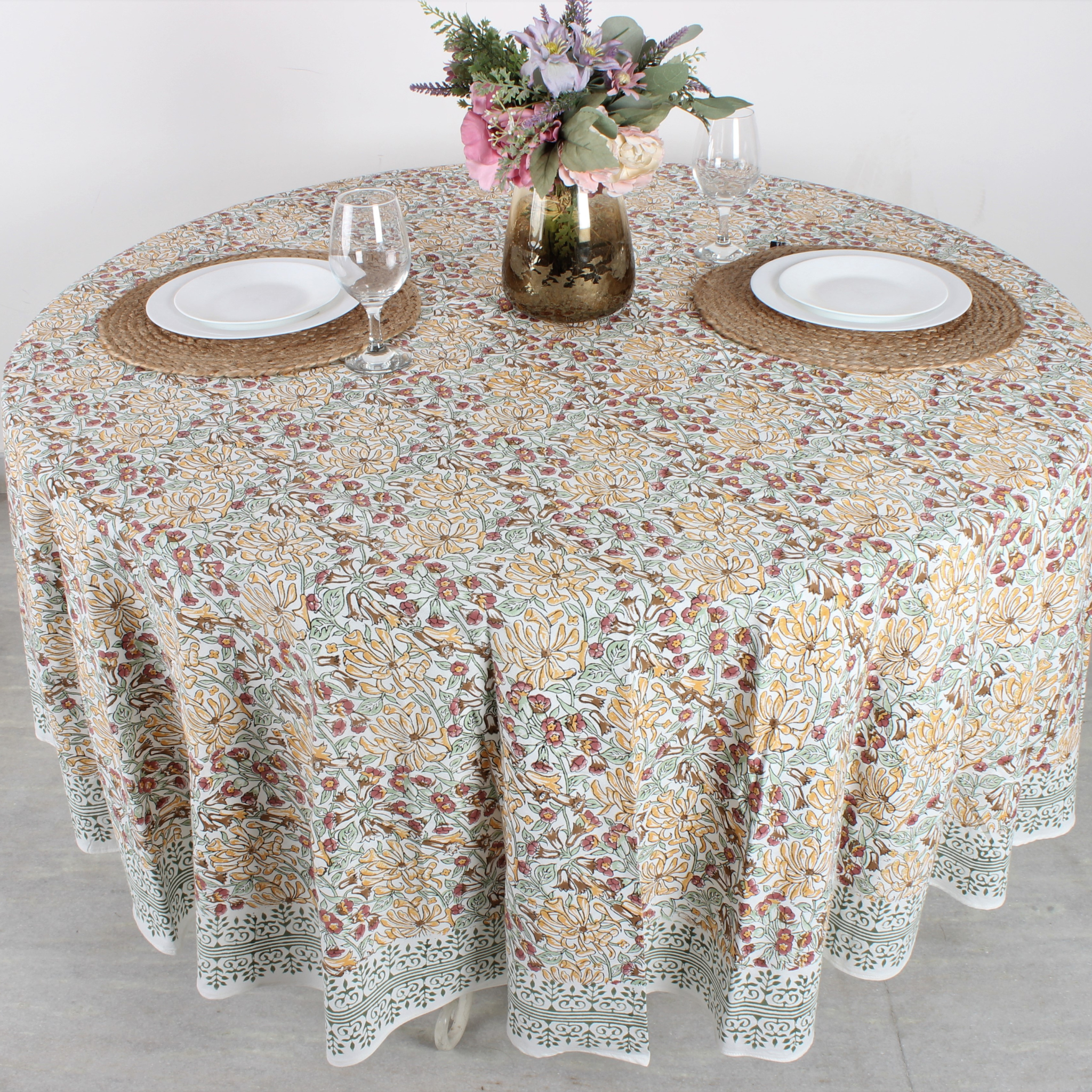 Round table with floral patterned tablecloth, plates, and glasses on a light background