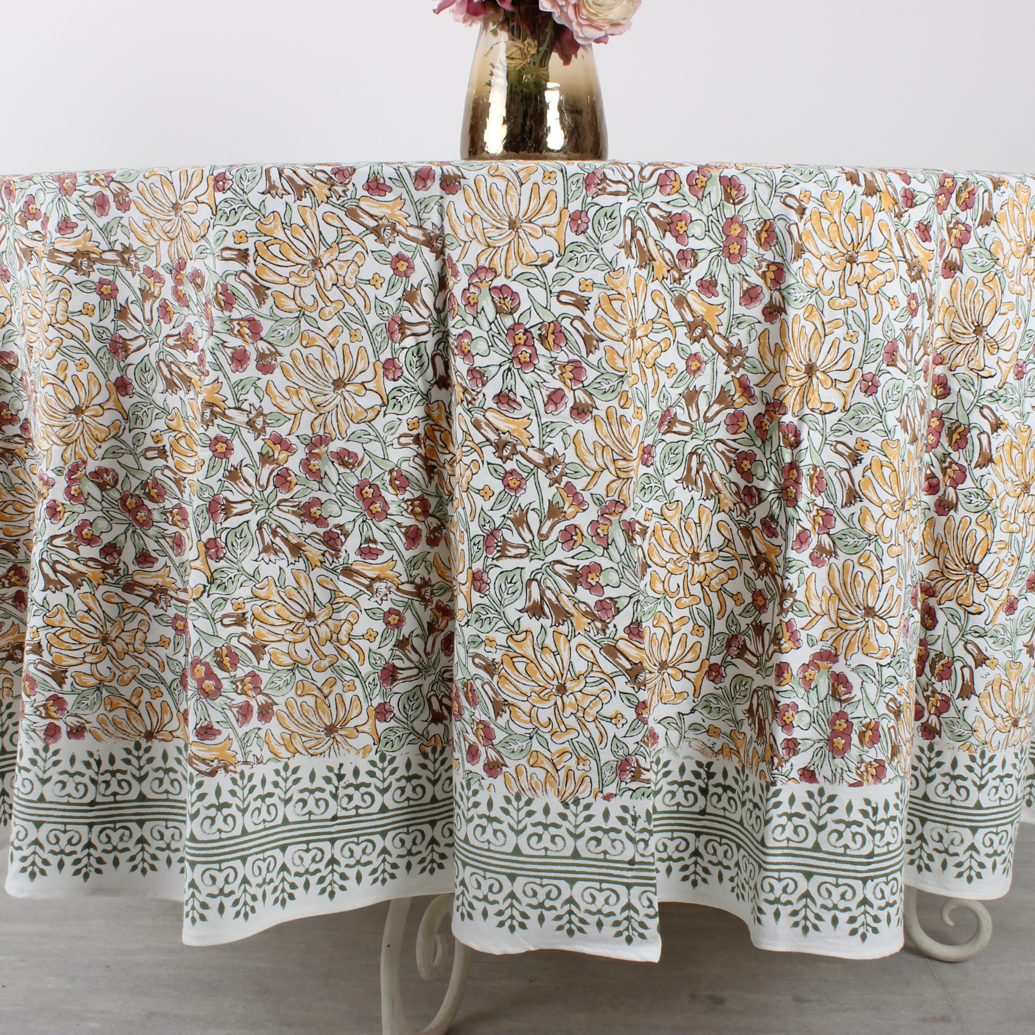 Floral patterned tablecloth on a round table with a vase of flowers.