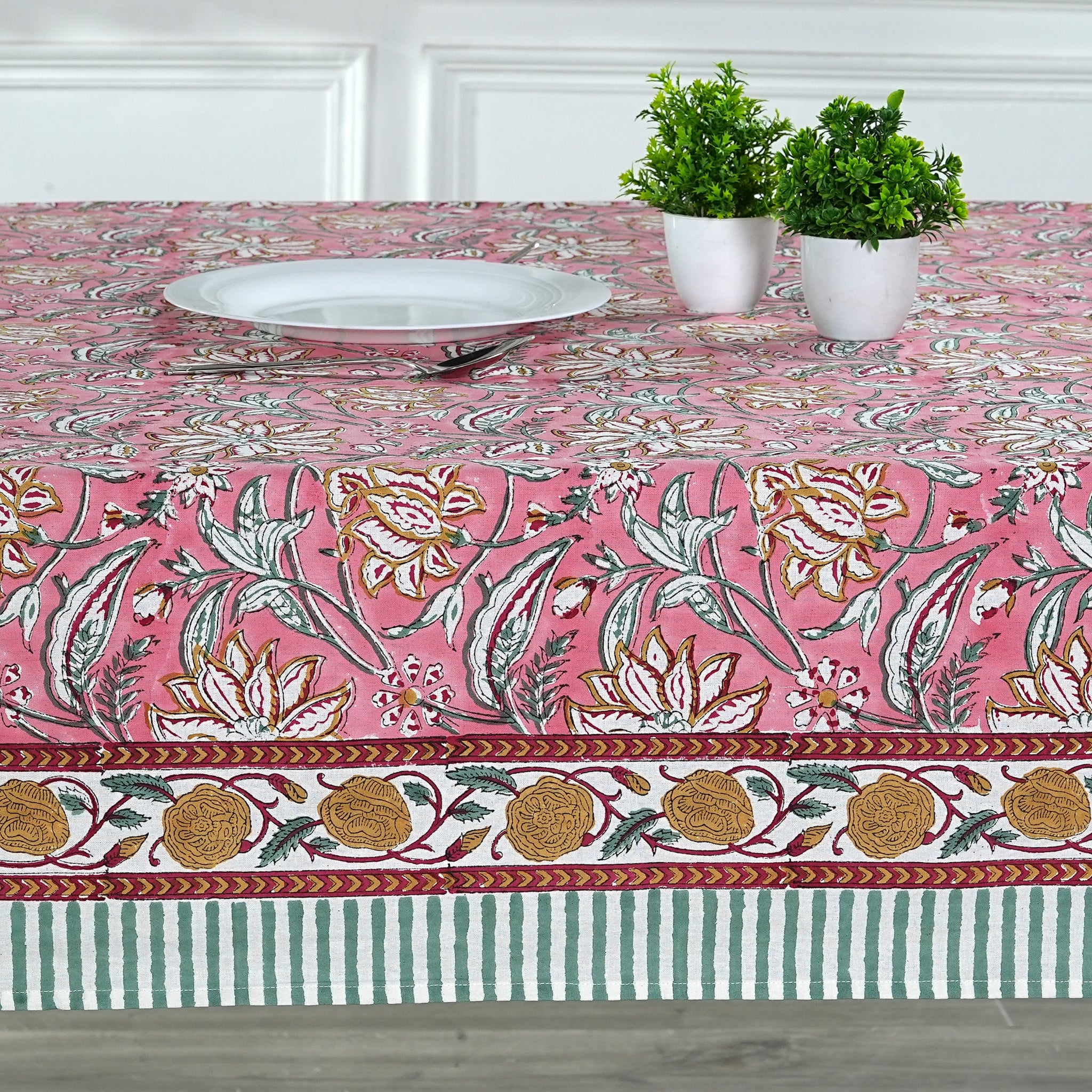 Tablecloth with floral and border design on a table with plates and plants.