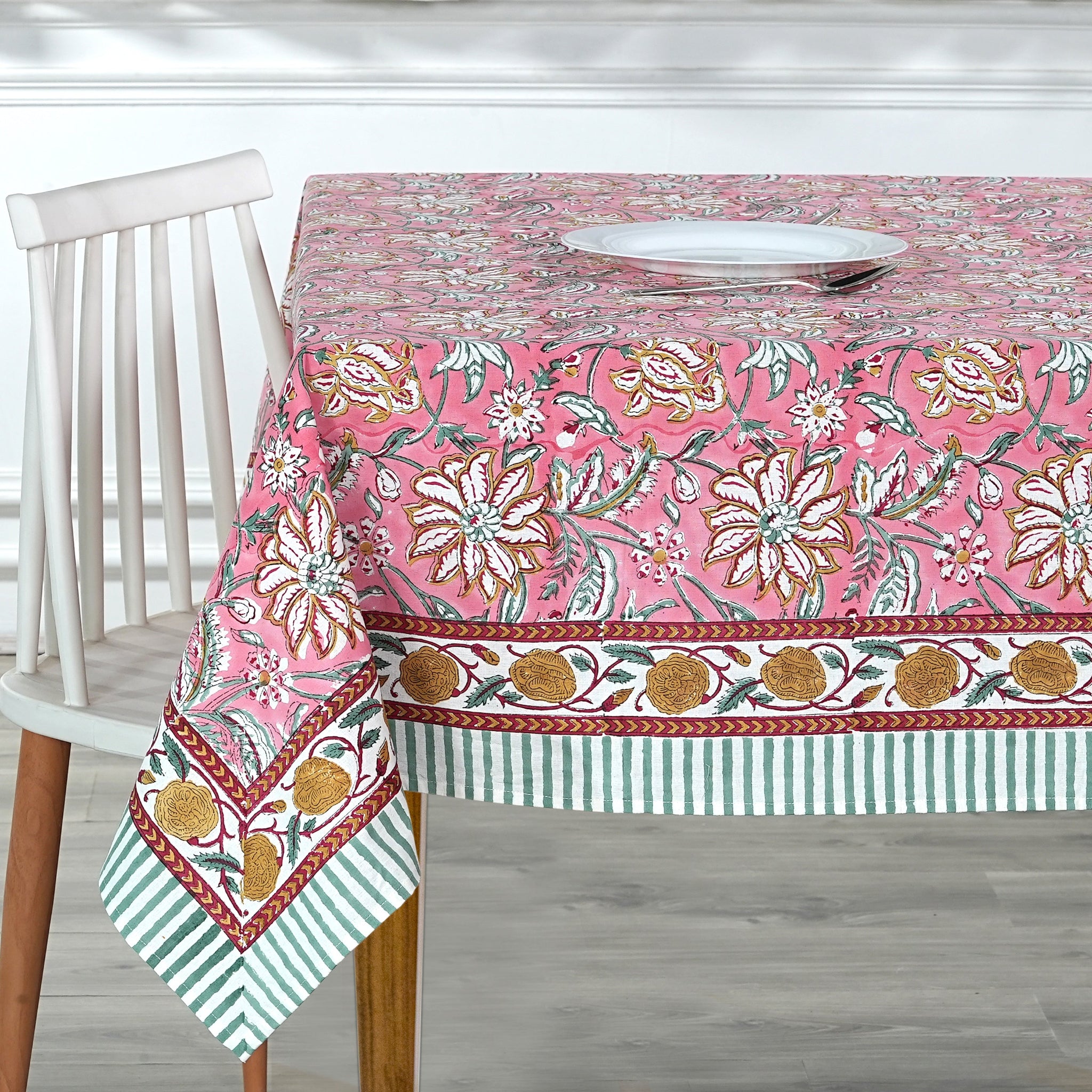 Floral patterned tablecloth on a wooden table with a white chair.