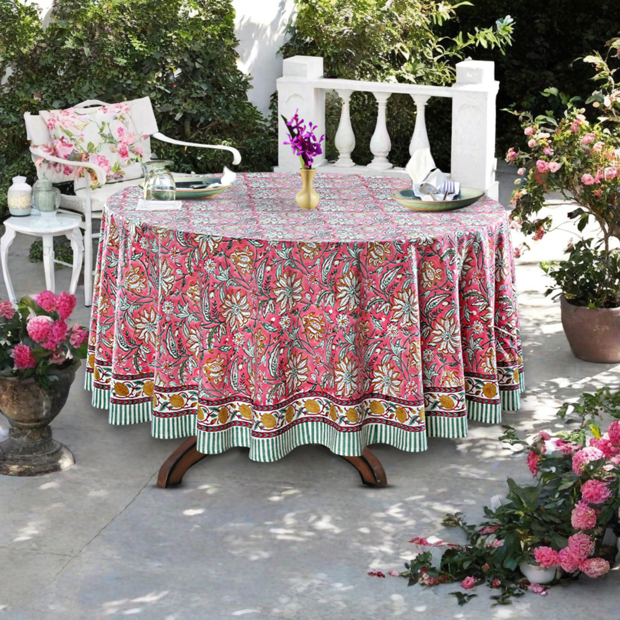 Outdoor setting with a floral tablecloth on a round table, surrounded by plants and chairs.