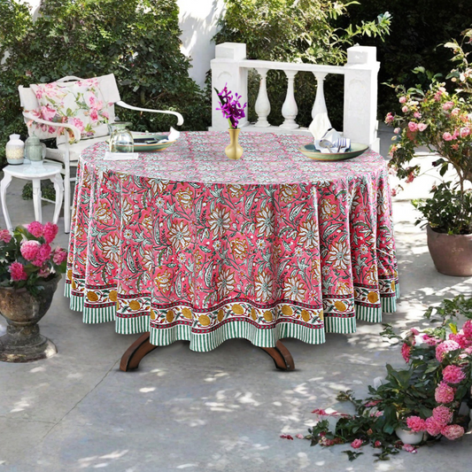 Outdoor setting with a floral tablecloth on a round table, surrounded by plants and chairs.
