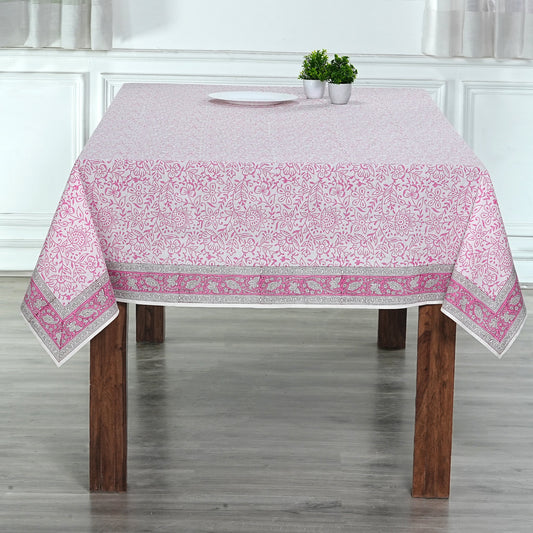 Tablecloth with pink floral pattern on a wooden table in a room with white walls.