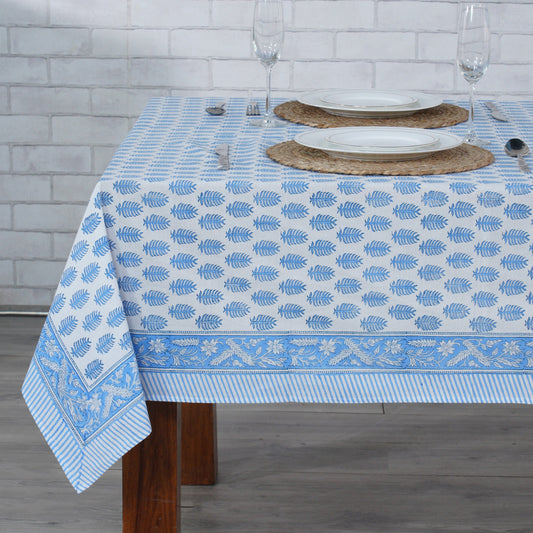 Tablecloth with blue leaf pattern on a dining table against a tiled wall.
