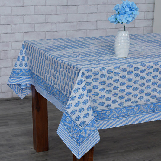 Blue and white patterned tablecloth on a wooden table with a vase of flowers against a brick wall.