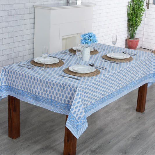 Dining table with a blue and white checkered tablecloth in a room with a fireplace and plants.