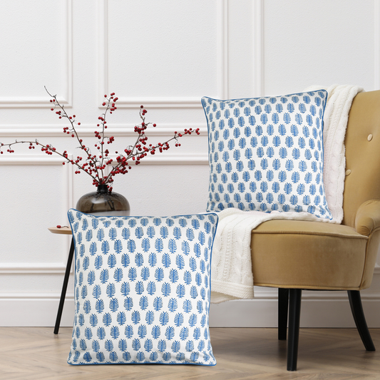 Two blue and white patterned pillows on a beige armchair with a vase of red berries on a side table.