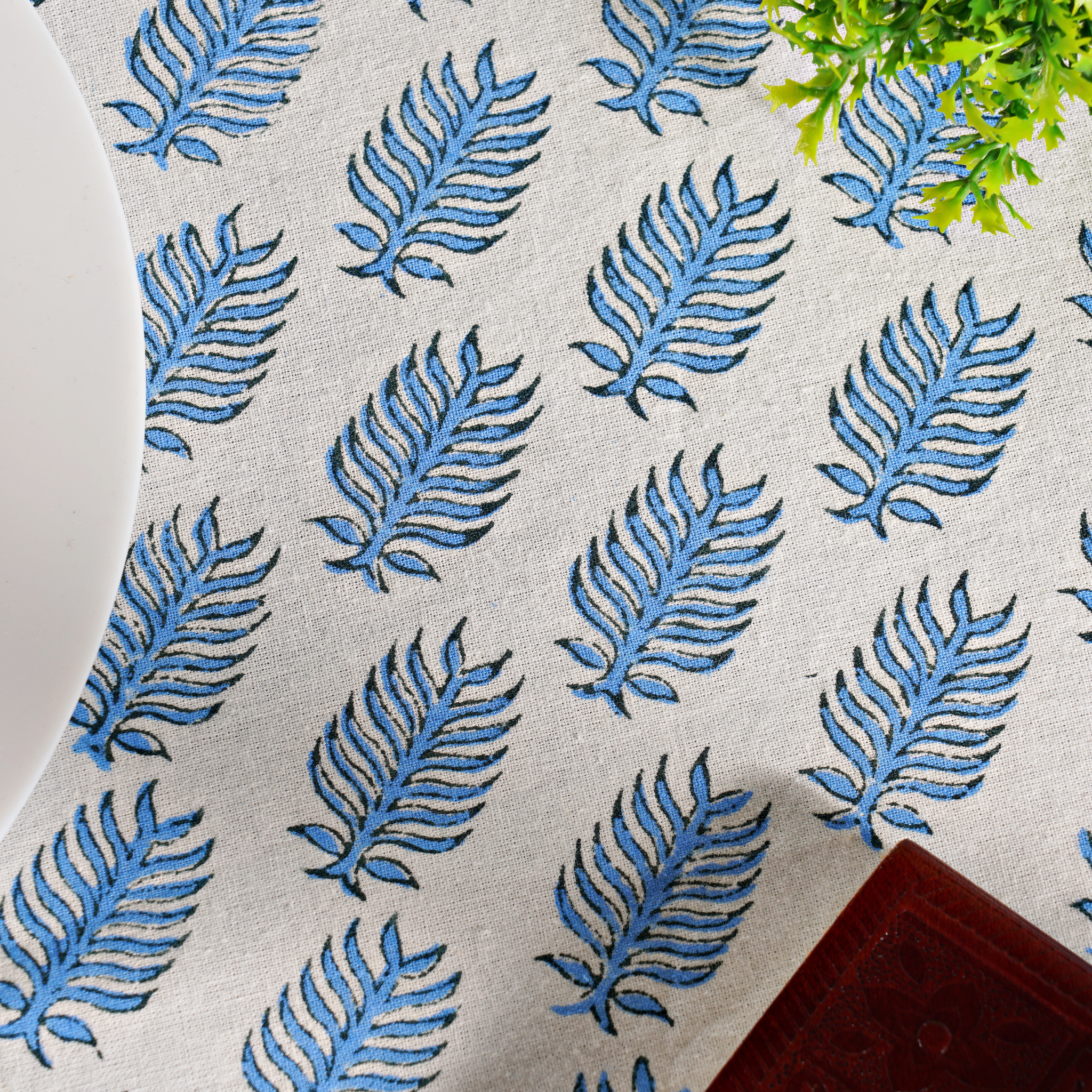 Pattern of blue leaves on a textured surface with a plant in the corner.
