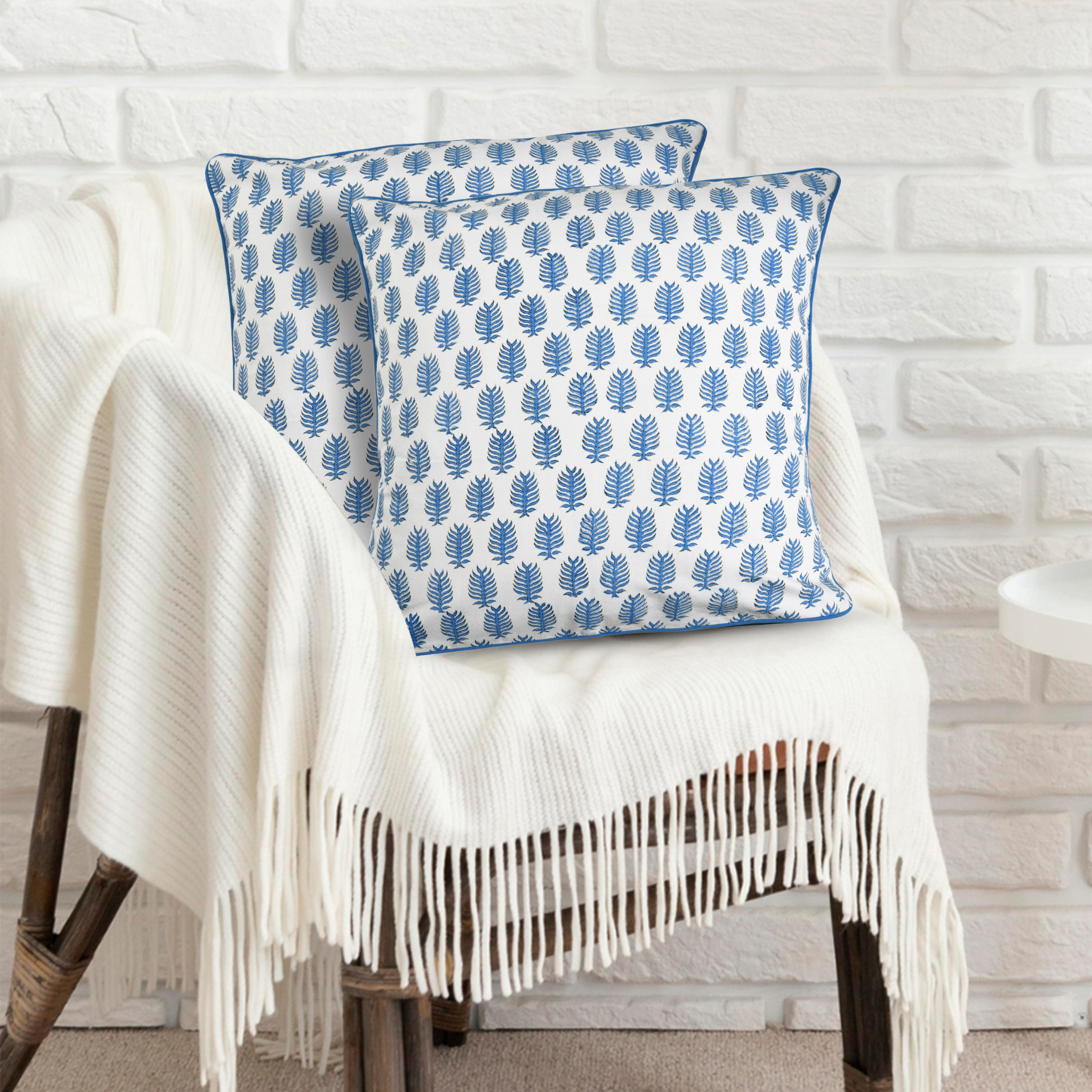 Two blue patterned pillows on a white chair with a white brick wall background