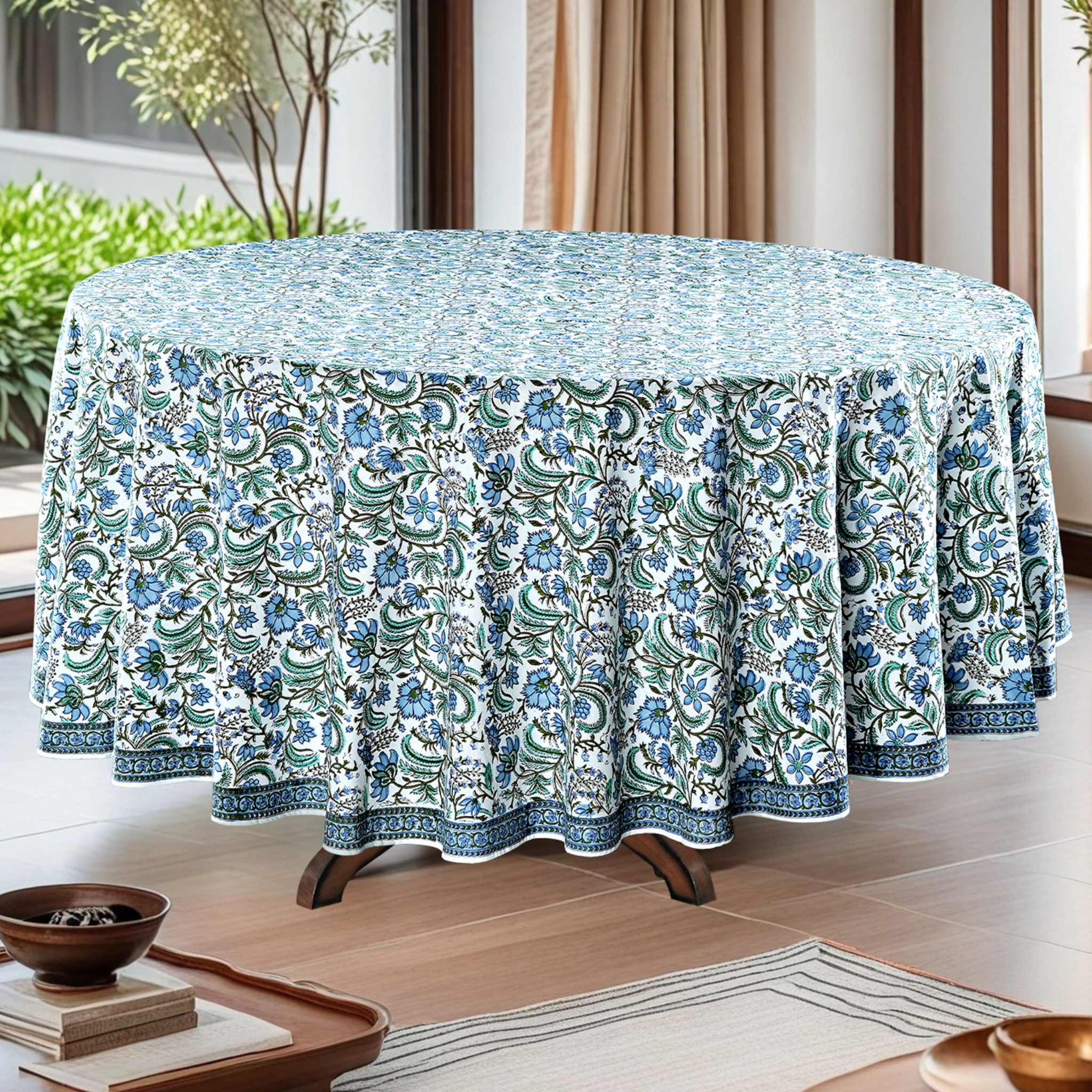 Round table with a floral patterned tablecloth in a room with plants and curtains.