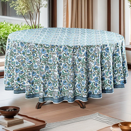 Round table with a floral patterned tablecloth in a room with plants and curtains.