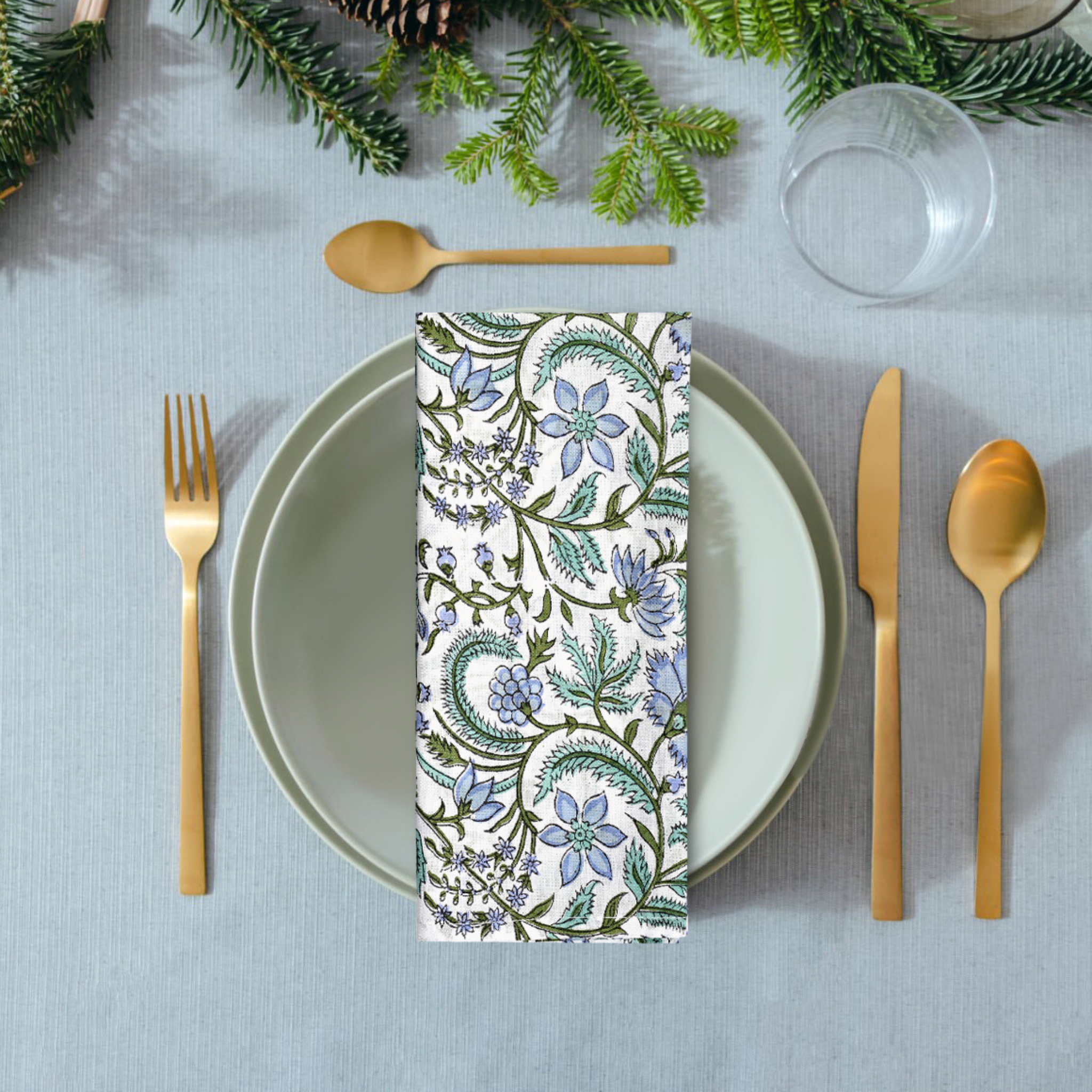 Napkin with floral pattern on a table setting with cutlery and greenery.