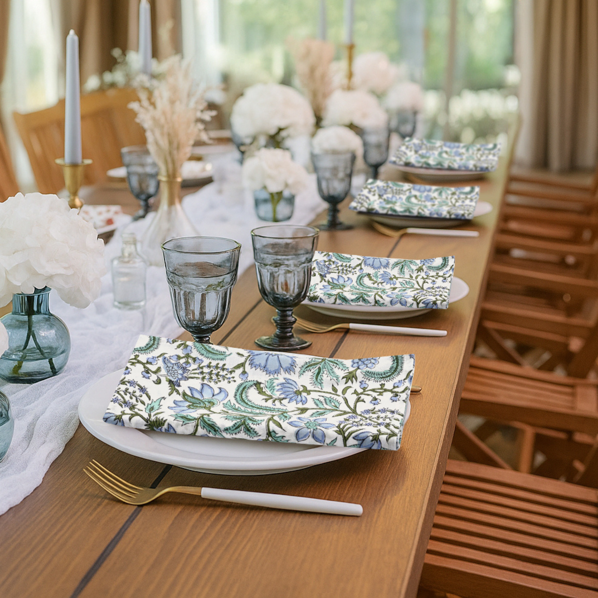 Dining table set with floral plates, glasses, and napkins in a bright room.