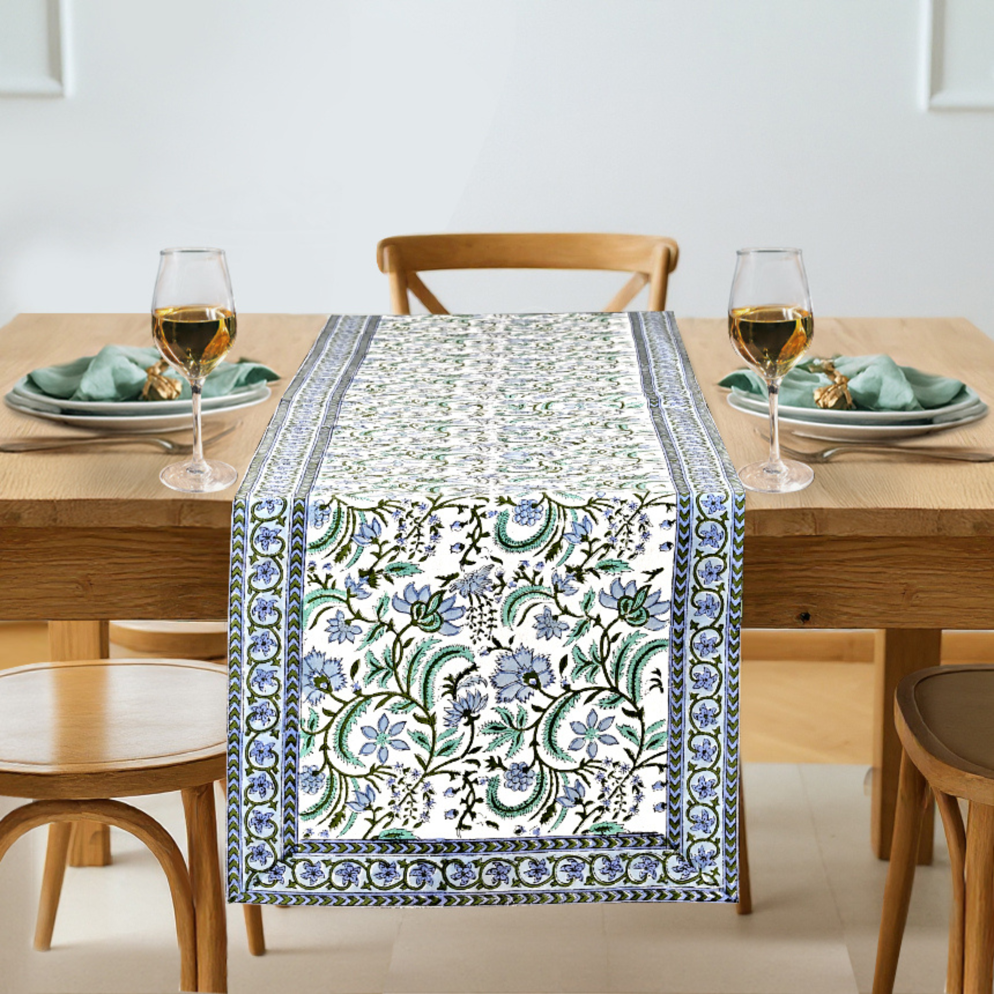 Dining table set with a floral patterned table runner, glasses, and plates.