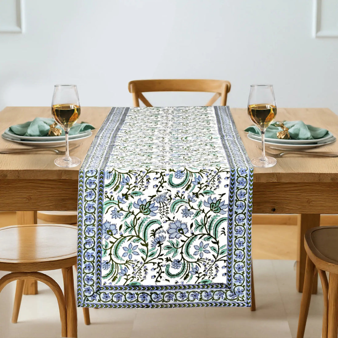 Dining table set with a floral patterned table runner, glasses, and plates.