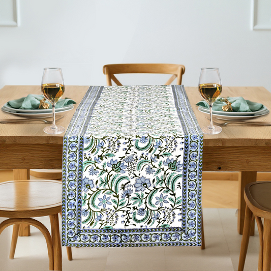 Dining table set with a floral patterned table runner, glasses, and plates.