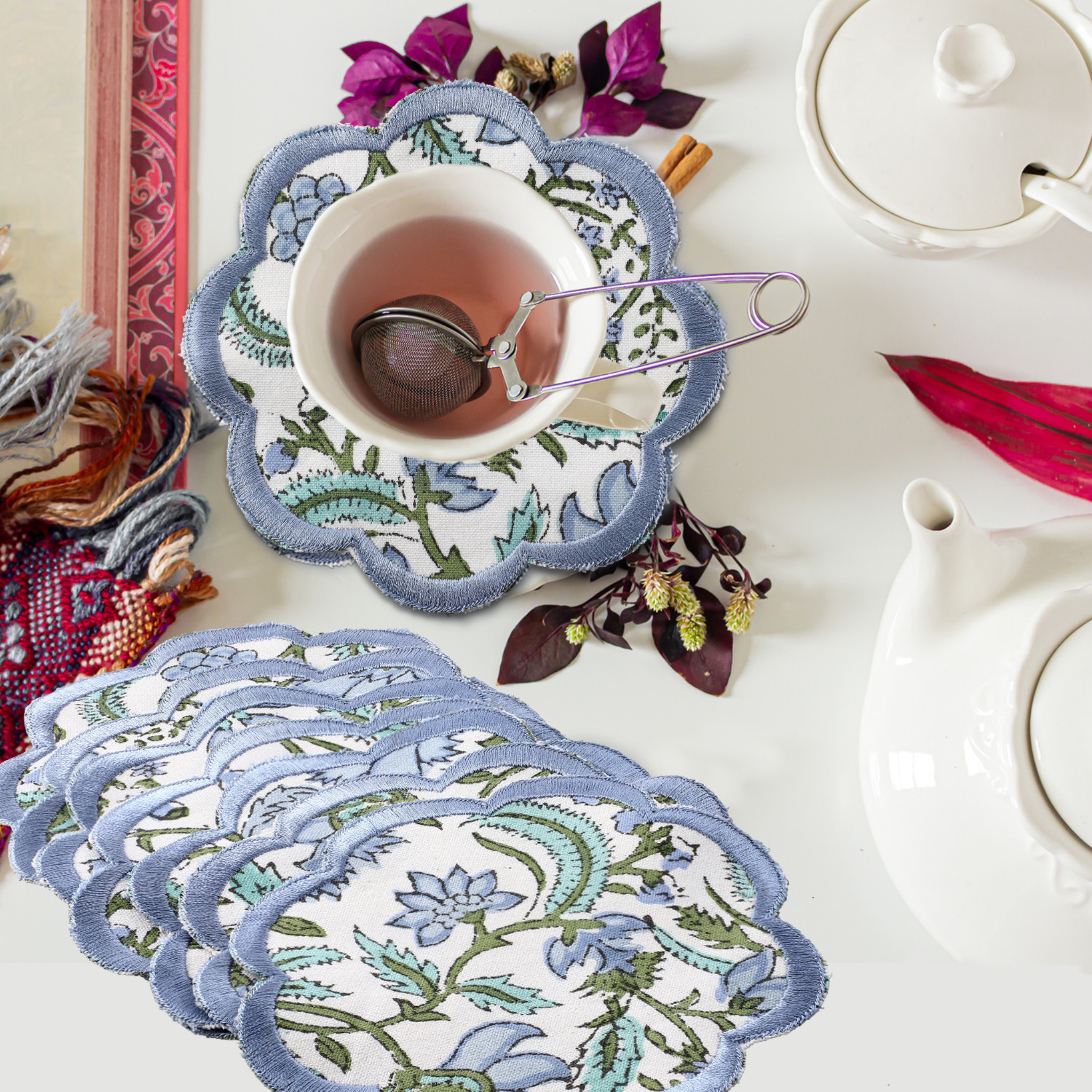 Set of floral coasters with a cup of tea and teapot on a table.