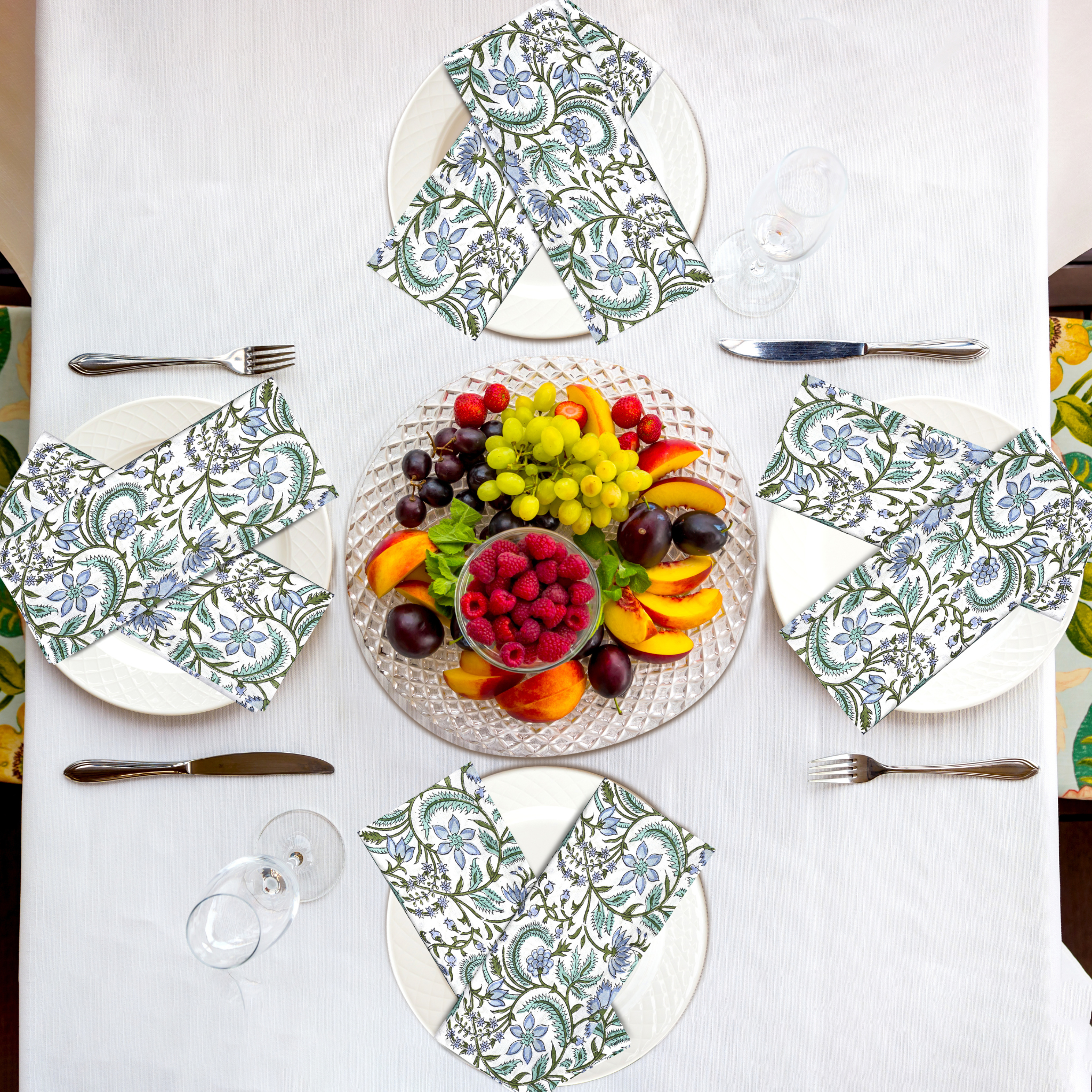 Table setting with patterned plates, napkins, and a fruit platter on a white tablecloth.