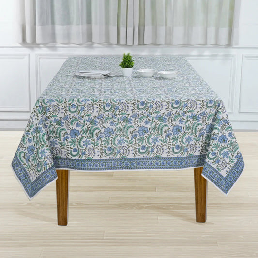 Tablecloth with floral pattern on a wooden table in a room with white walls and curtains.