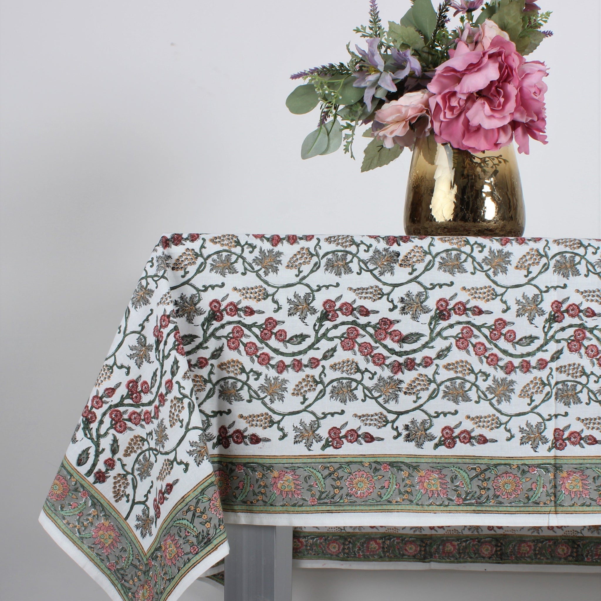 Decorative tablecloth with floral pattern on a table, accompanied by a vase of flowers.