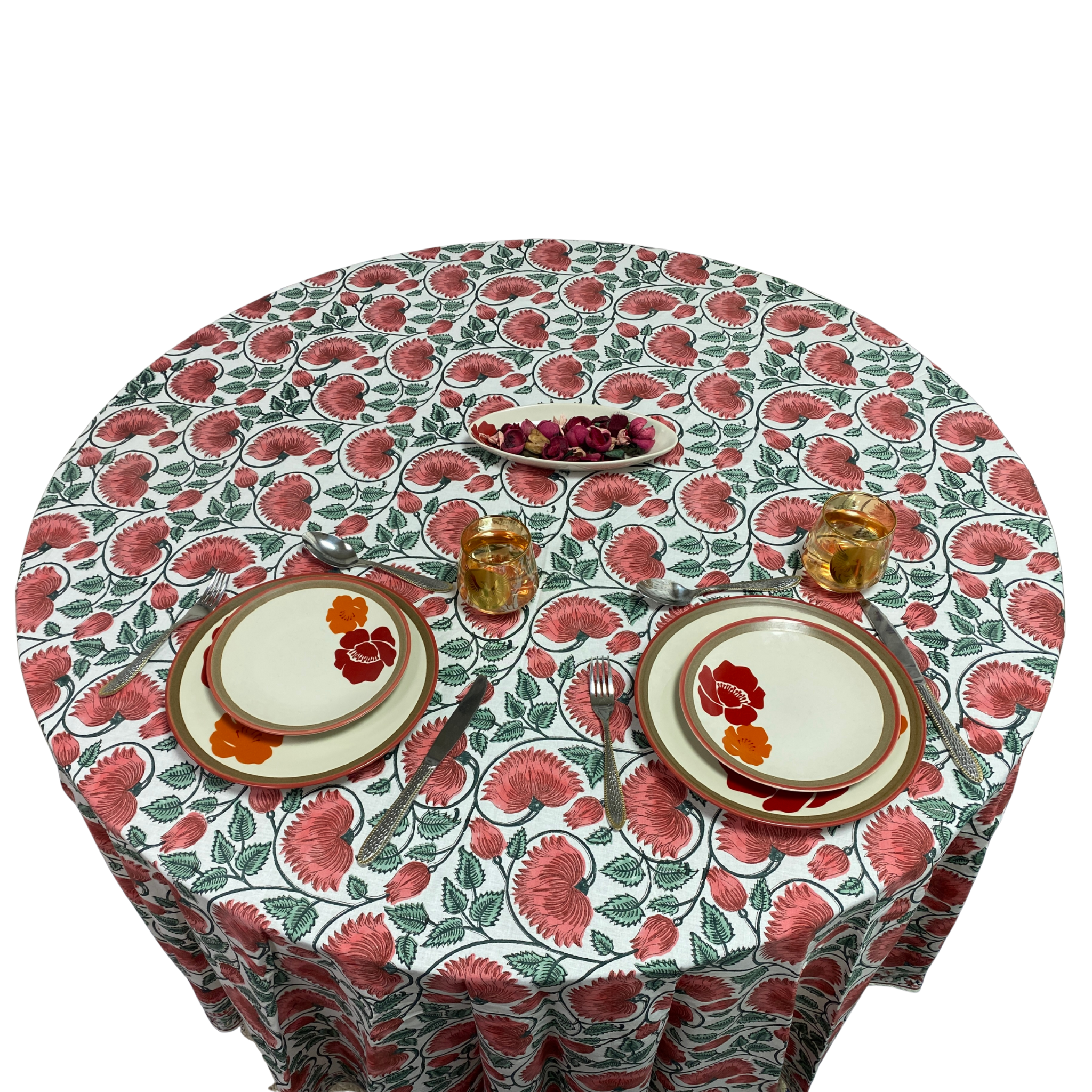 Round table with floral patterned tablecloth set for two with plates, cutlery, and glasses.