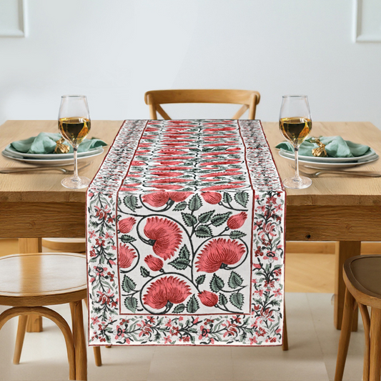 Floral table runner on a dining table with glasses and plates.