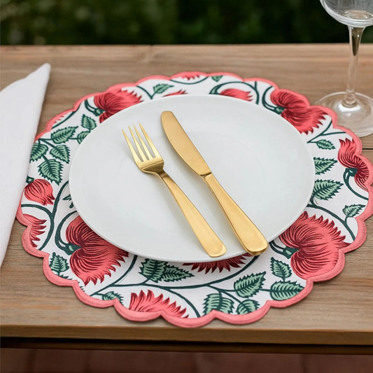 Placemat with floral design, white plate, gold fork and knife on a wooden table.