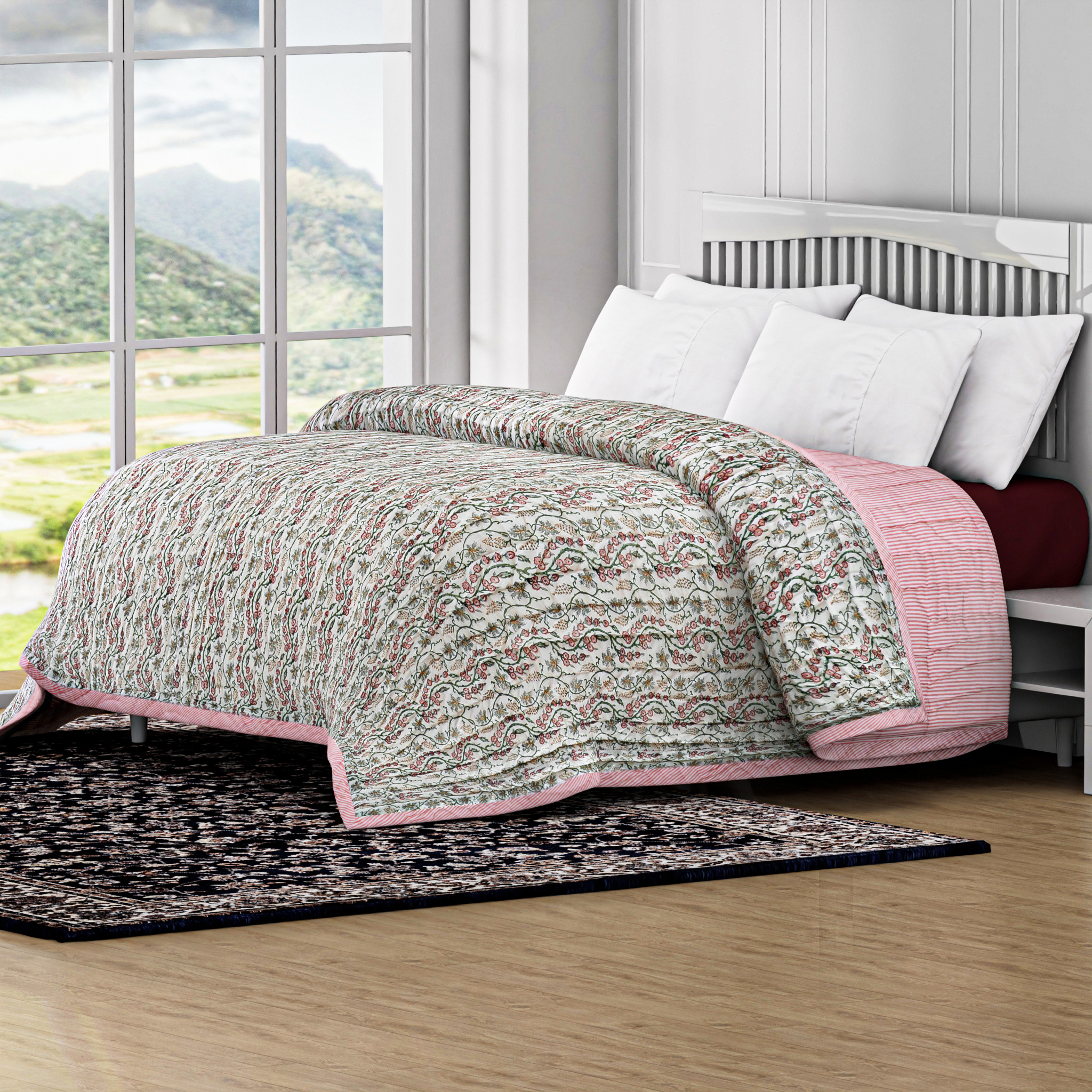 Bed with floral quilt and pink accent in a room with large windows showing a scenic view.