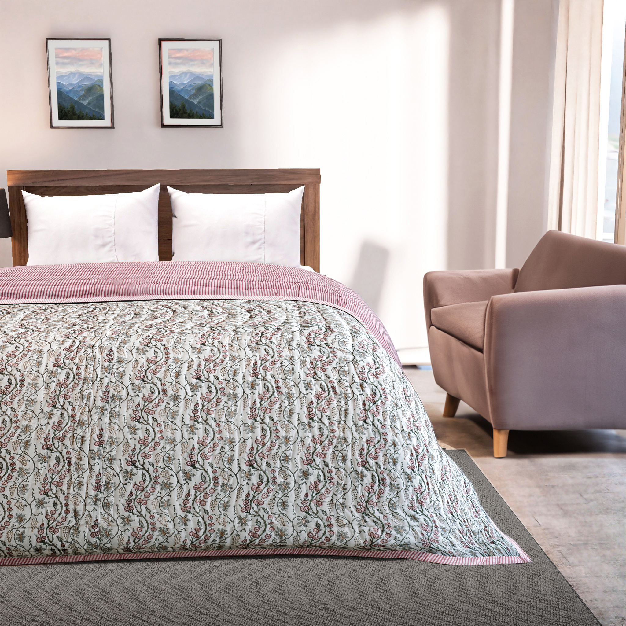 Bedroom with a bed covered in a patterned quilt, a chair, and framed pictures on the wall.