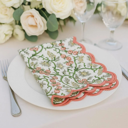 Decorative floral napkin on a white plate with flowers and glasses in the background
