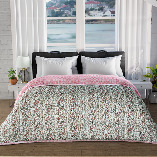 Bed with pink and green patterned comforter in a room with large windows showing a view of water and buildings.