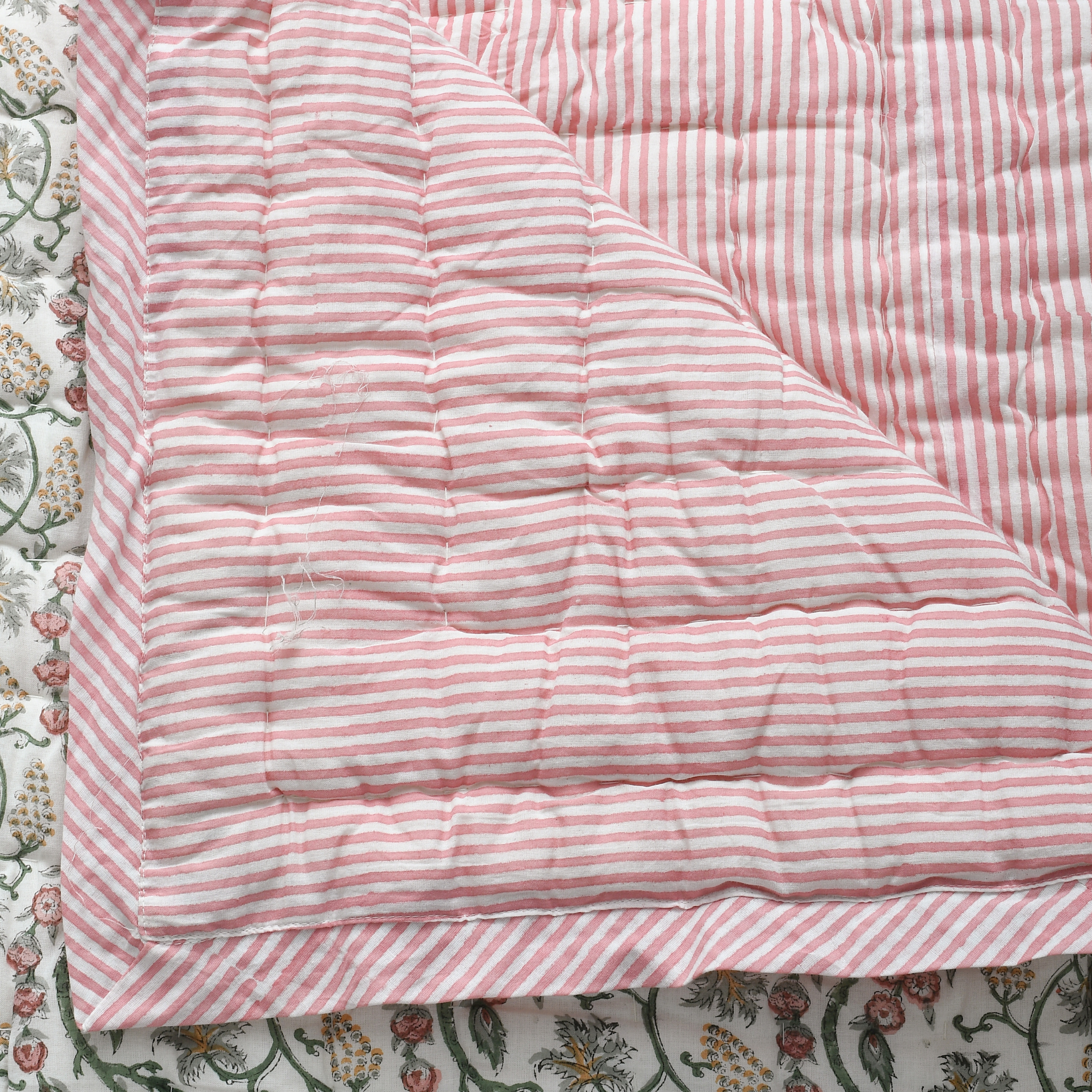 Pink and white striped quilt on a floral bedspread