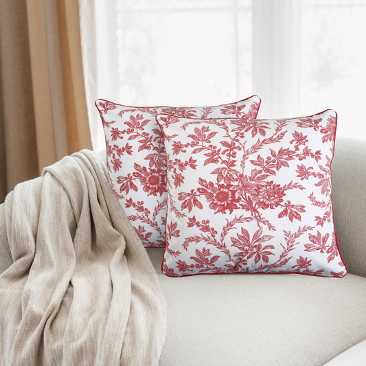 Two red floral patterned pillows on a beige couch with a neutral curtain in the background.