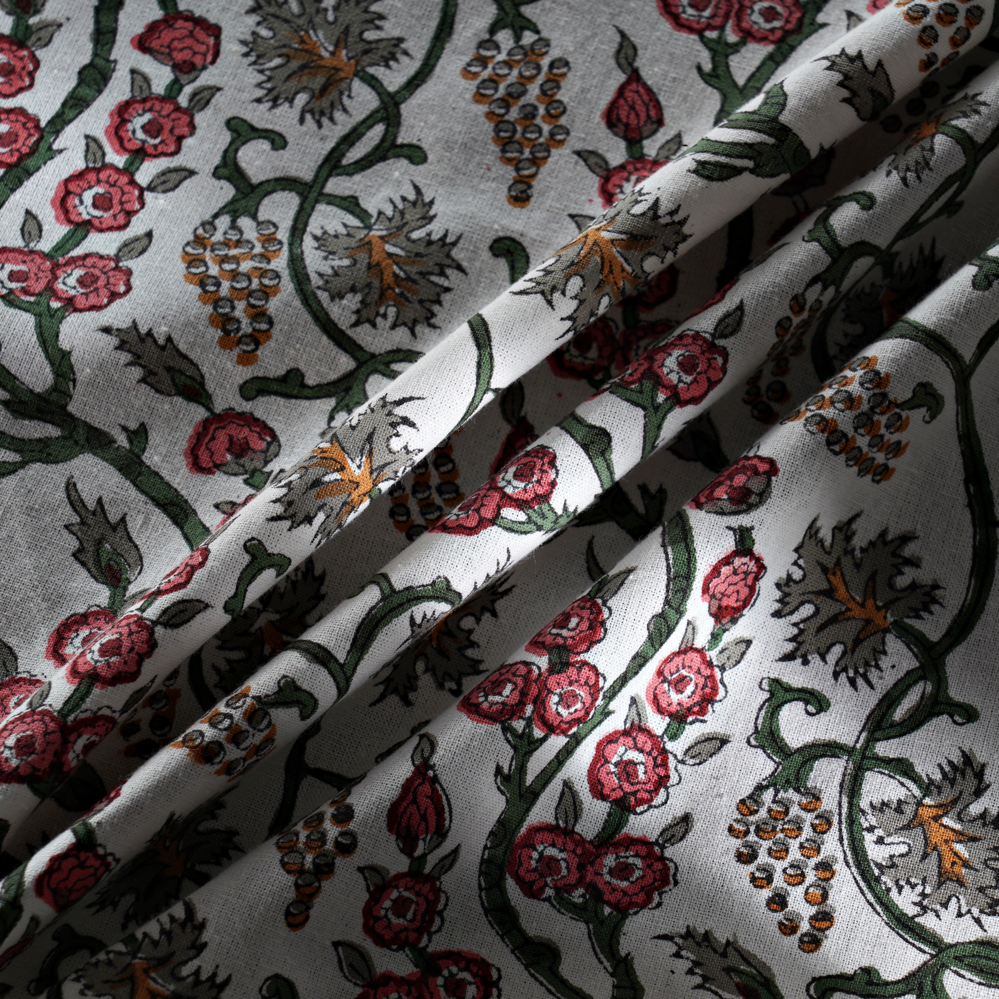 Floral and vine patterned fabric with red flowers and green leaves on a white background.