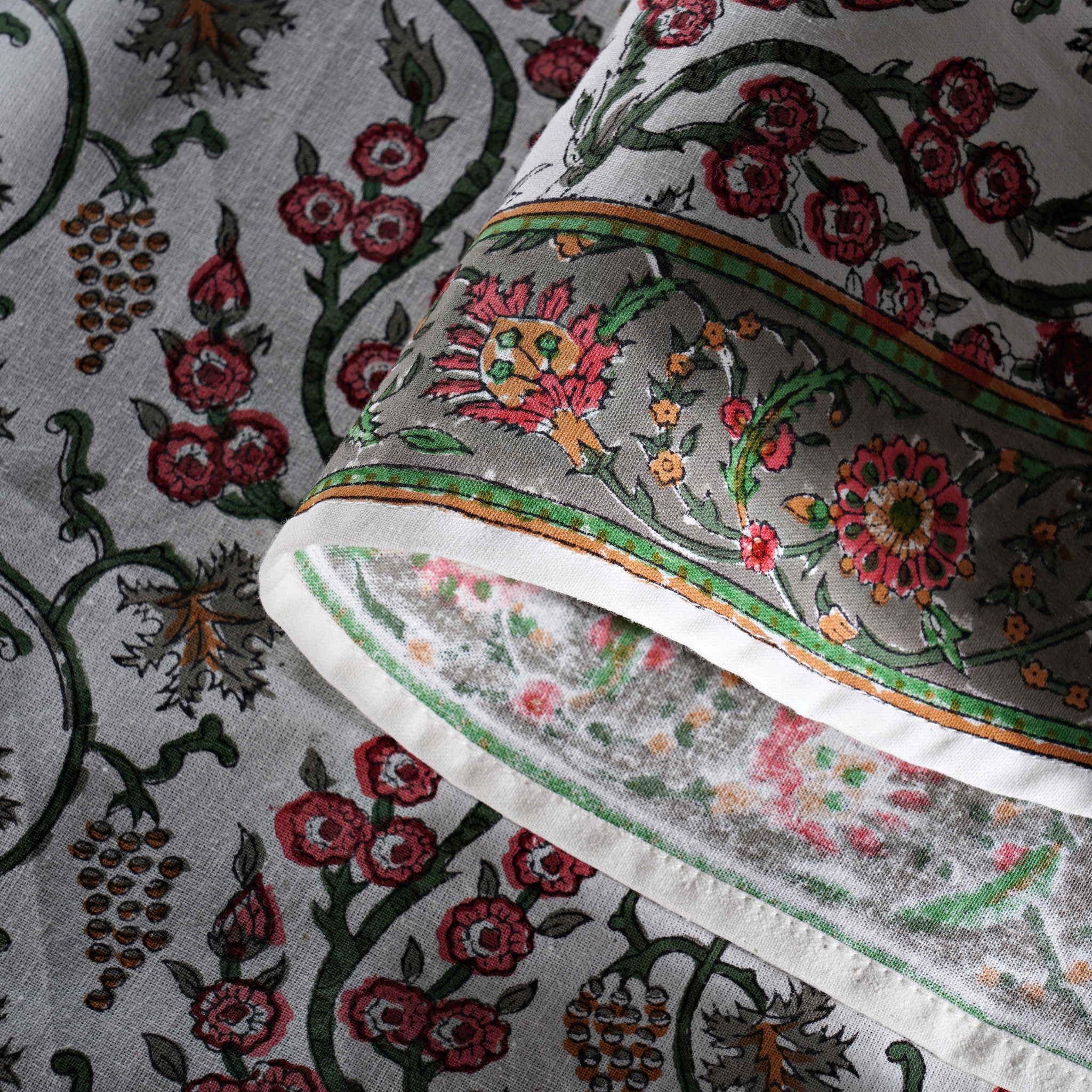 Close-up of a fabric with intricate floral and vine patterns on a gray background.