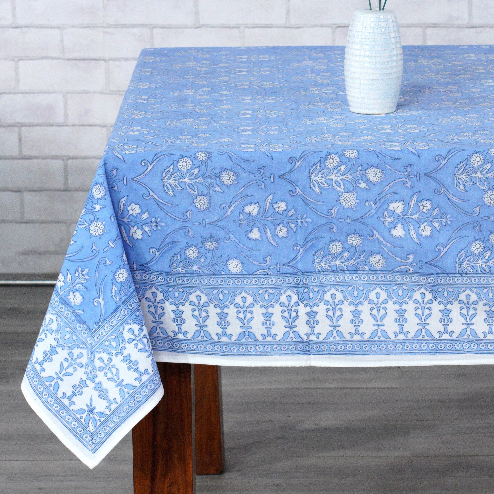 Blue floral patterned tablecloth on a wooden table with a white vase.