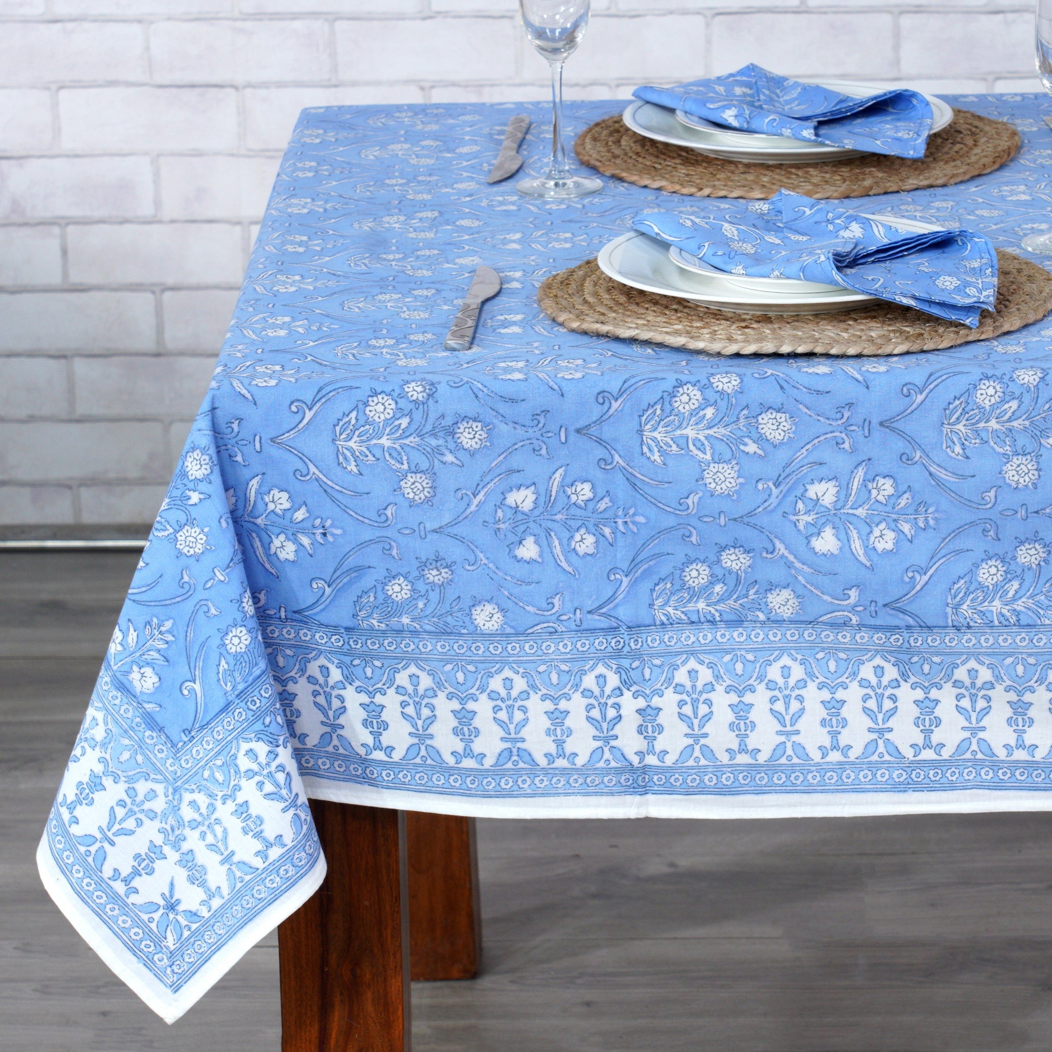 Table setting with a blue floral-patterned tablecloth on a wooden table.