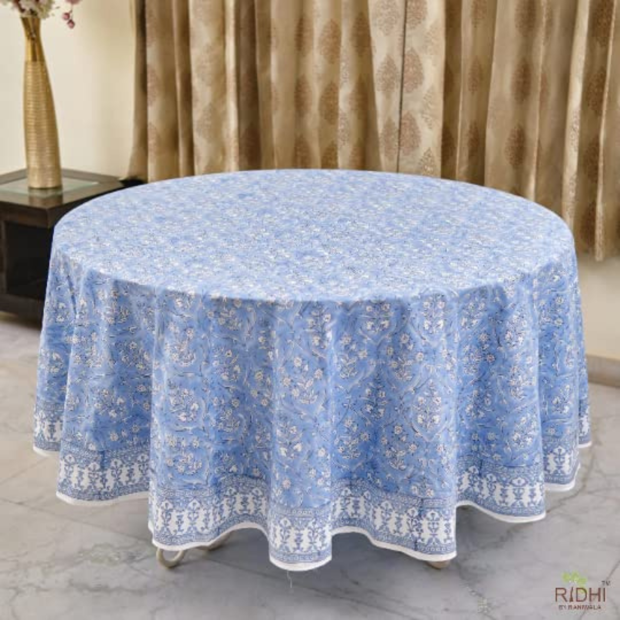Round table covered with a blue floral tablecloth in a room with curtains.