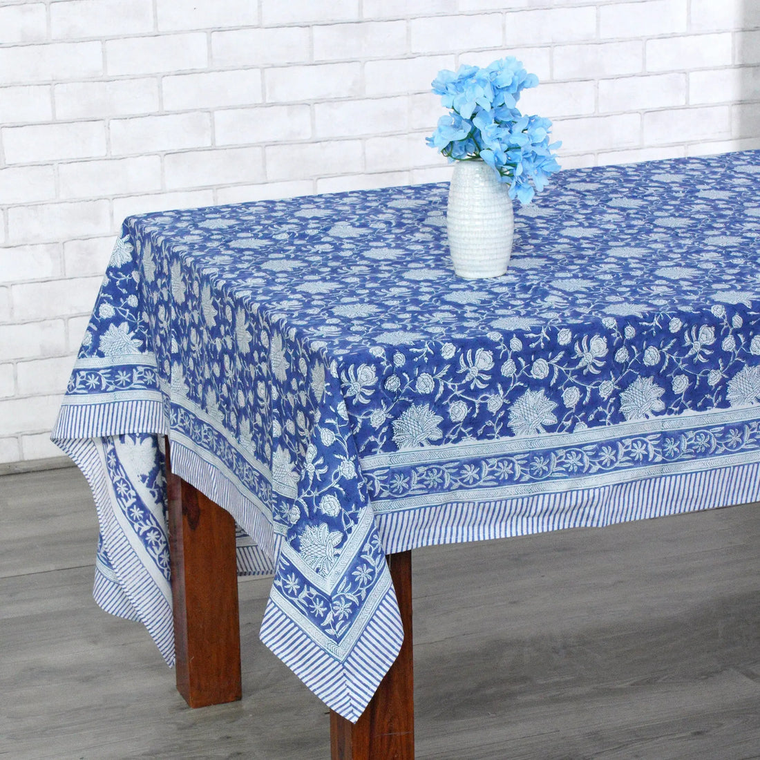 Table with a blue floral patterned tablecloth against a white brick wall.