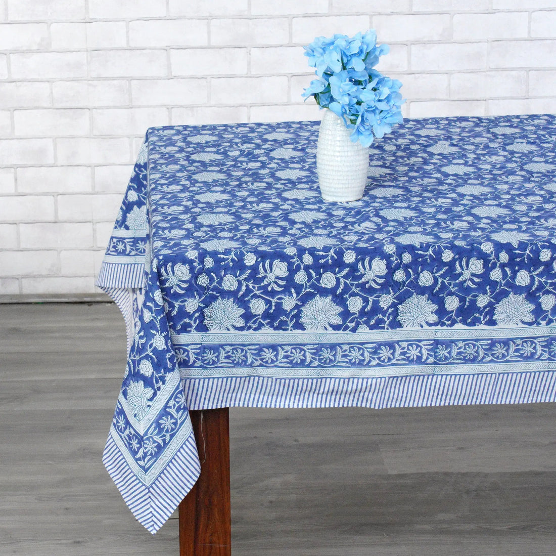 Table with a blue floral tablecloth against a white brick wall.