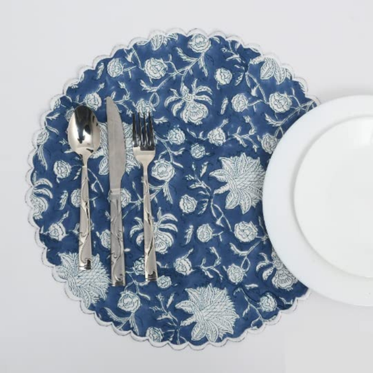 Blue floral-patterned placemat with silverware and a white plate on a white background