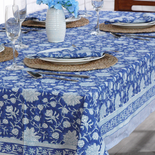 Dining table set with blue floral tablecloth, plates, and cutlery.