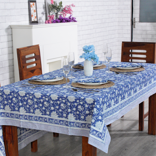 Dining table set with a blue floral tablecloth in a room with white brick walls.