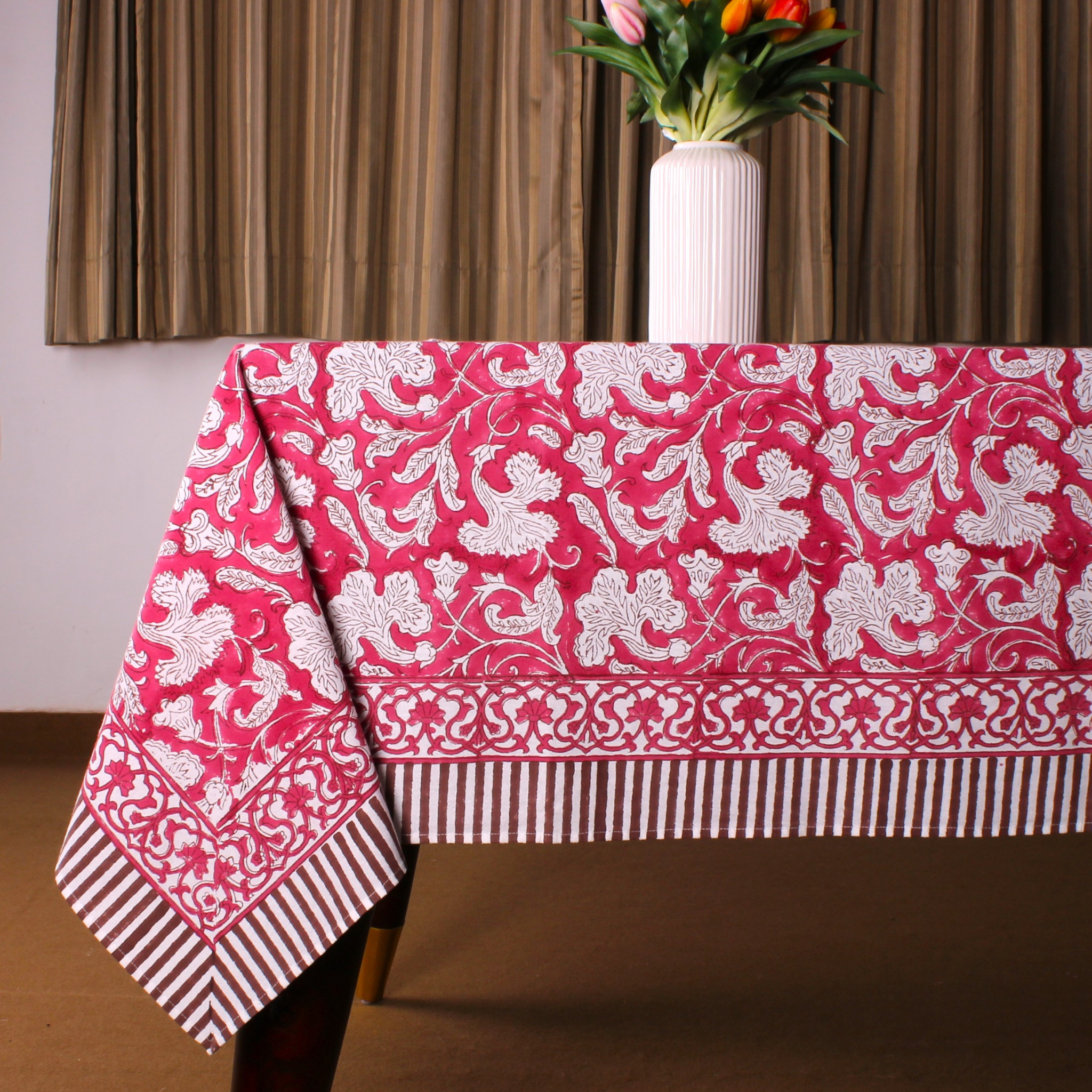 Pink tablecloth with white floral pattern on a table, with a vase of flowers in the background.