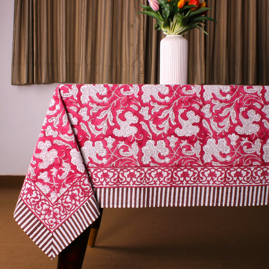 Pink tablecloth with white floral pattern on a table, with a vase of flowers in the background.